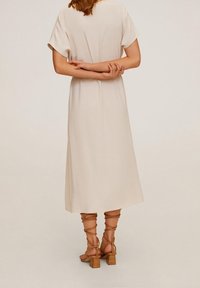 Robe midi beige à manches courtes et coupe décontractée, avec une texture lisse. Modèle portant des sandales tan à brides avec des talons carrés.
