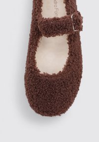 Brown Mary Jane shoe made of textured fabric with a rounded toe and secured strap featuring a metal buckle. Soft, fuzzy material.
