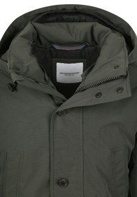 Olijfgroene jas met hoge kraag, zwarte hardware, ritssluiting en knoopdetails. Label met de tekst "McGregor" en het oprichtingsjaar 1951.