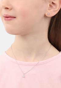 Silberne Halskette mit einem kleinen, klaren Edelstein-Anhänger, getragen mit passenden Ohrsteckern, kombiniert mit einem hellrosa Shirt.