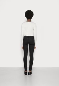 Top blanco de manga larga combinado con jeans skinny negros. Tejido suave con un diseño ajustado. Zapatos negros completan el look.