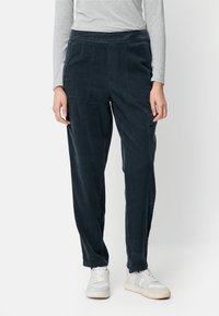 Marineblaue Cordhosen mit elastischem Bund, Seitentaschen und verjüngten Beinen, kombiniert mit weißen Turnschuhen. Glatte Textur, lässiges Design.