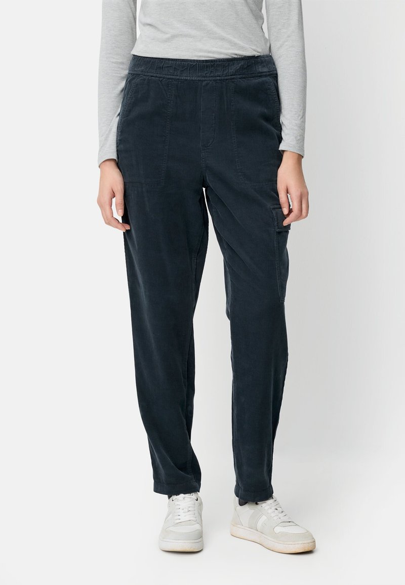 Marineblaue Cordhosen mit elastischem Bund, Seitentaschen und verjüngten Beinen, kombiniert mit weißen Turnschuhen. Glatte Textur, lässiges Design.