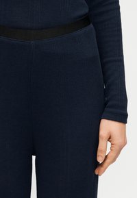 Μπλε ναυτικό ριμπ πλεκτό τοπ με μακριά μανίκια και εφαρμοστή γραμμή, με μαύρη ελαστική ζώνη στη μέση, που αναδεικνύει υφή υφάσματος και στενή εφαρμογή στον καρπό.