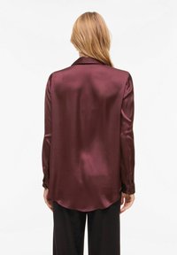 Blouse en satin bordeaux à manches longues avec un ourlet arrondi, dotée d'un col classique et de poignets à boutons, texture lisse. Vue de dos montrée.