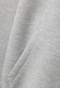 Lichtgrijze sweatshirtstof met een zachte textuur. Heeft een kanga pocket en een subtiel, geweven patroon door het materiaal.