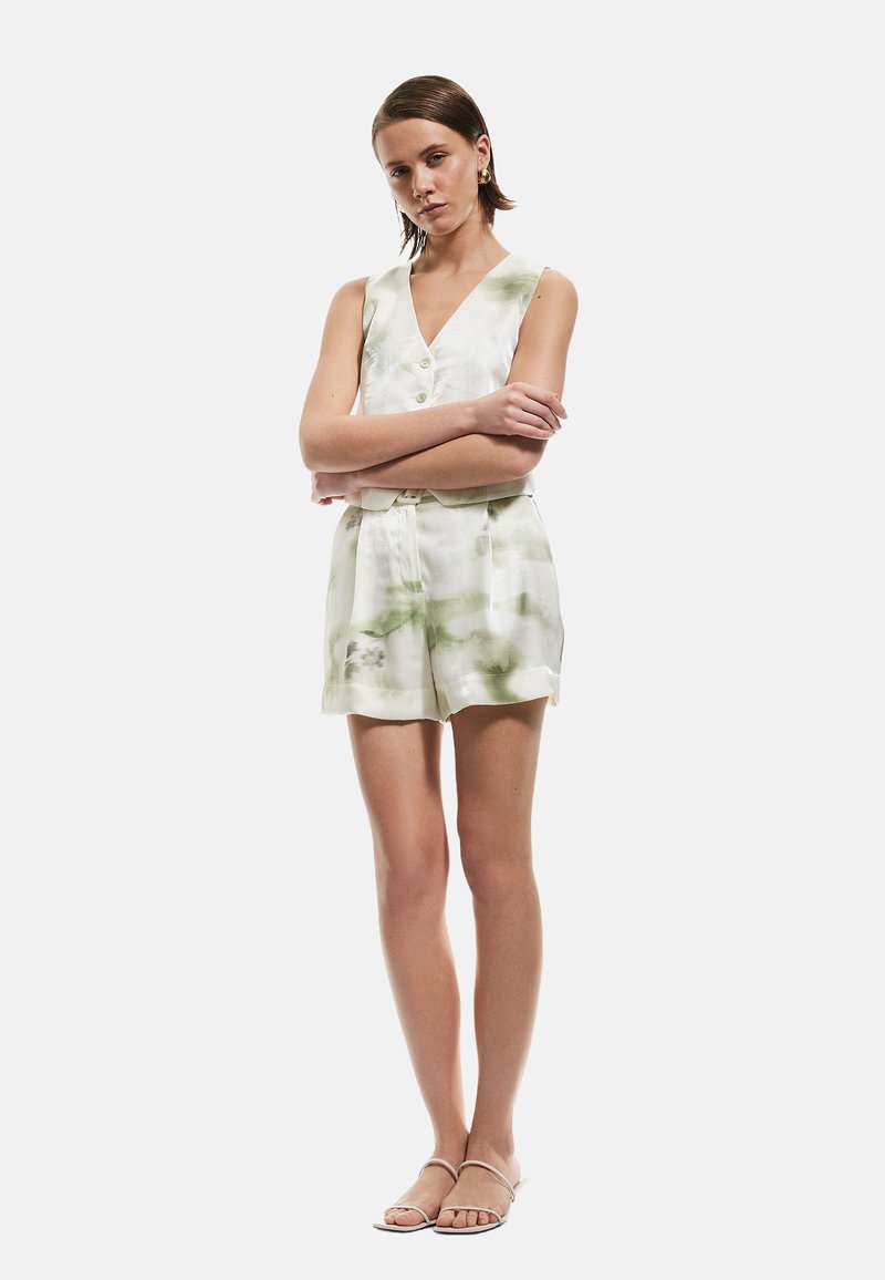 Mono sin mangas en tonos blanco y verde con estampado tie-dye, con escote en V, botones al frente y bolsillos laterales, combinado con sandalias minimalistas.