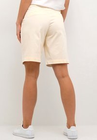 Krémové bavlněné kraťasy s rovný fit, do délky kolen, s dvojitým švem na lemech a zadními kapsami. Nosené s bílými teniskami.