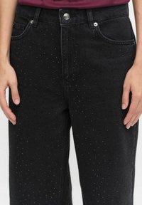 Czarne dżinsy o luźnym kroju, charakteryzujące się teksturowaną powierzchnią ozdobioną małymi, błyszczącymi ćwiekami oraz standardowymi kieszeniami z przodu.