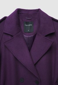 Cappotto viola doppiopetto con ampio revers, realizzato in tessuto testurizzato. Presenta bottoni neri e una fodera interna liscia. Etichetta del marchio visibile.