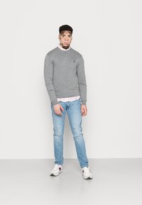Grijze trui met lange mouwen, gelaagd over een witte en roze gestreepte shirt, gecombineerd met lichtblauwe jeans en witte sneakers.