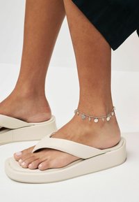 Beige platform sandaler med en bred tårem. Sølv anklet med små runde charms. Glat tekstur og minimalistisk design.