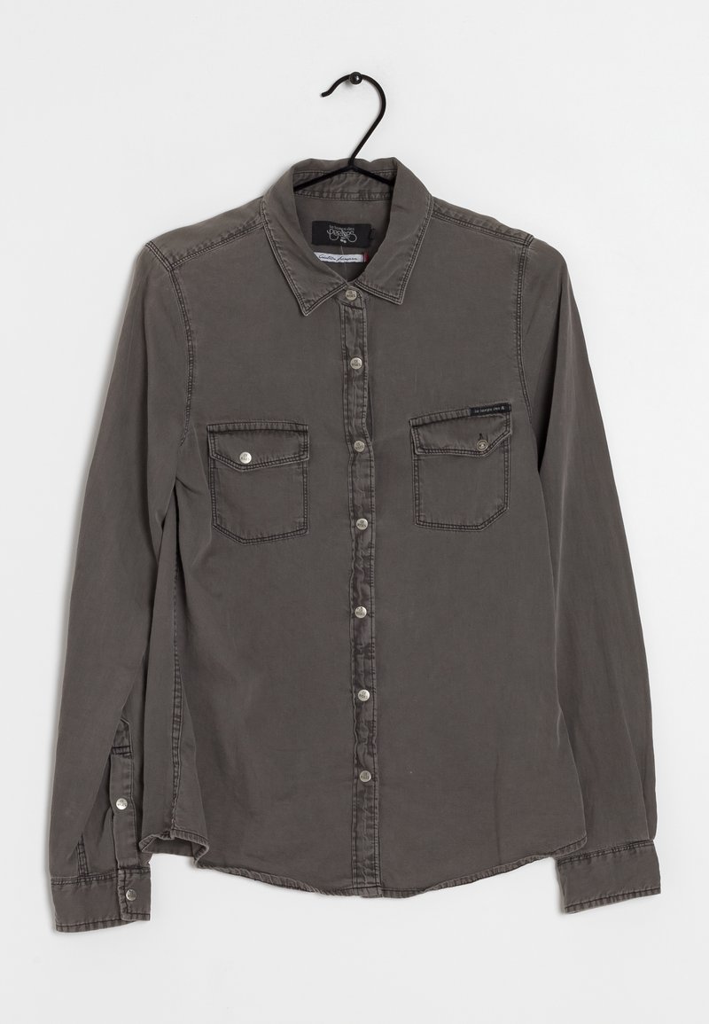 Chemise gris foncé à manches longues avec boutons sur le devant, deux poches poitrine, boutons visibles et col, suspendue sur un cintre noir sur fond blanc.