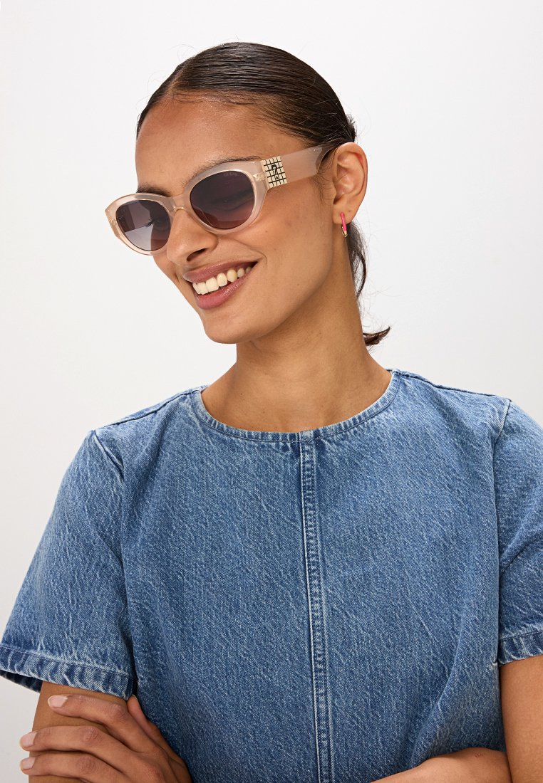 Helle rosa Sonnenbrille im Cat-Eye-Style, dunkeltönte Gläser und dekorative Verzierungen an den Bügeln. Glatte, glänzende Oberfläche.