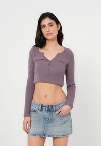 Μωβ ριμπ κοντό τοπ με μακριά μανίκια και στρογγυλή λαιμόκοψη, με λεπτομέρειες κουμπιών, σε συνδυασμό με φούστα μίνι από ανοιχτό μπλε τζιν.