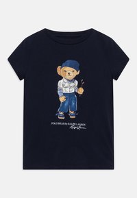 Námorně modré bavlněné tričko s podrobnou ilustrací medvěda v volnočasovém oblečení, který drží golfové hole, a s nápisem "Polo Bear by Ralph Lauren" pod obrázkem.