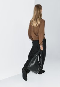 Borsa hobo in pelle nera con una superficie liscia e una sola tracolla, abbinata a un maglione marrone e pantaloni neri larghi.