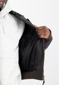 Svart läderjacka med en vadderad svart foder, med ribbade bruna manschetter och en guldfärgad dragkedja. Bärs över en grå hoodie.