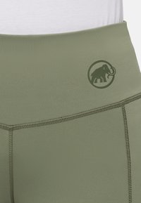Olijfgroene high-waisted leggings van rekbare stof, met een olifantlogo in een cirkelontwerp en zichtbare flatlockstiksels.