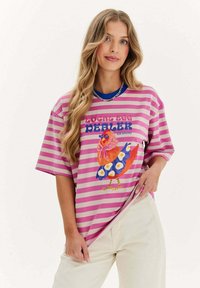 Pruhované oversize tričko v růžové a bílé barvě s barevným potiskem kohouta v modrých šatech a květinovými akcenty. 100% bavlna, krátké rukávy.