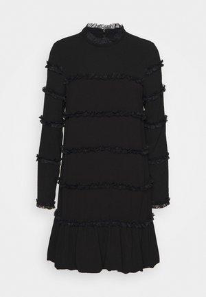 Czarna sukienka z długimi rękawami, z falbaniastymi warstwami na tułowiu i rozkloszowanym dołem. Dekolt i mankiety rękawów mają koronkowe wykończenie.