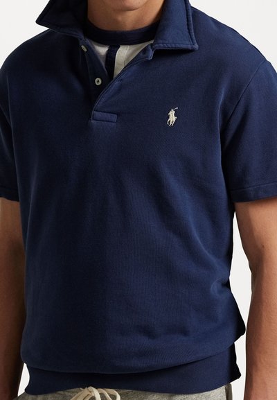 Navy blue polo shirt with a knitted collar, two-button placket, and embroidered logo on the left chest. Soft fabric and relaxed fit.
