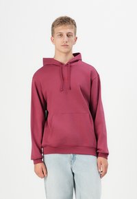 Maroon hooded sweatshirt with a front pocket, featuring a plain design and ribbed cuffs. Paired with light blue denim jeans.