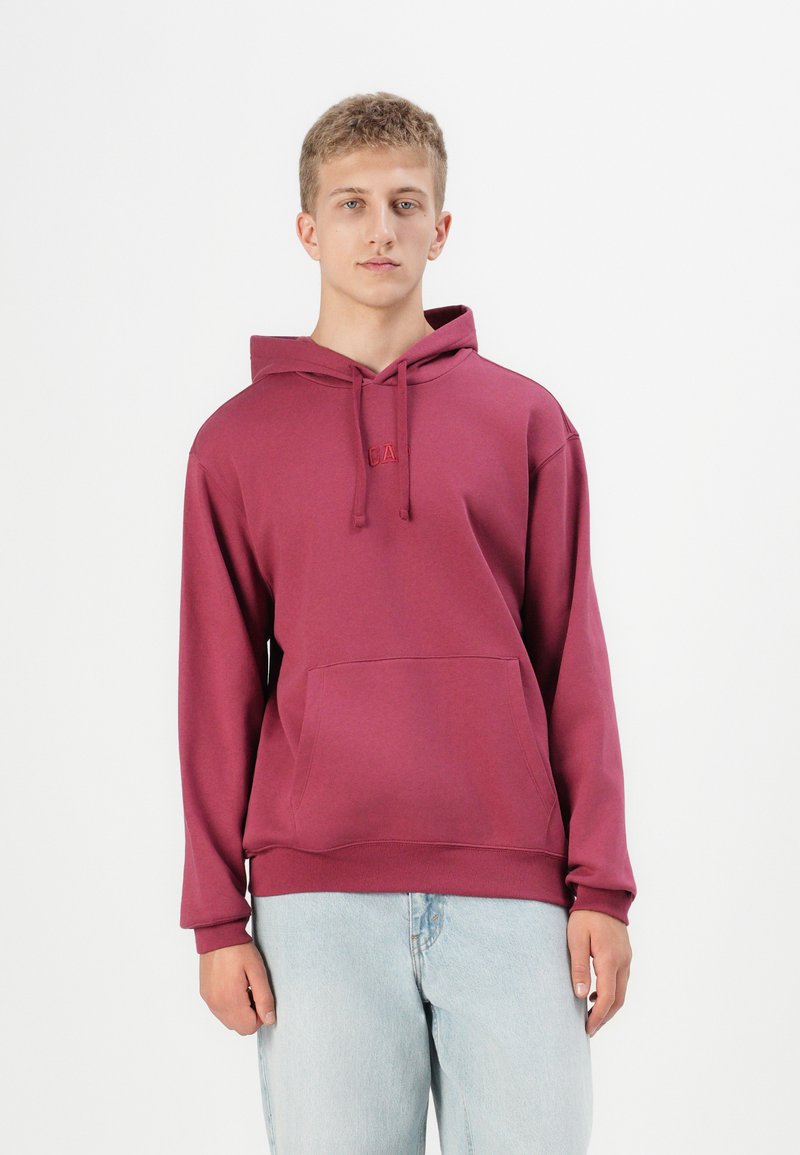 Maroon hooded sweatshirt with a front pocket, featuring a plain design and ribbed cuffs. Paired with light blue denim jeans.
