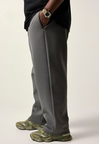 Grå sweatpants med sidelommer, tætsiddende pasform og en glat tekstur. Sammen med olivengrønne sneakers med netdetaljer.