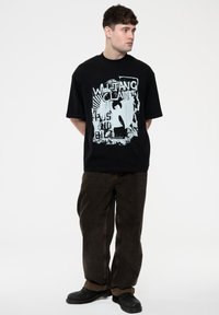 Black oversized t-shirt featuring a graphic print of "Wu-Tang Clan" in light blue, paired with dark brown pants and black shoes.