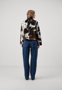 Braun-weiß gemusterte Kalbslederjacke mit Stehkragen, kombiniert mit blauen Jeans. Rückansicht wird gezeigt.