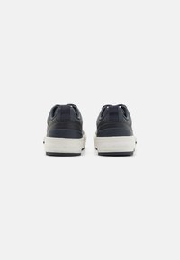 Marineblaue Leder-Sneaker mit einer weißen Gummisohle, ausgestattet mit doppelten Zuglaschen und gesteppten Akzenten an der Ferse. Einfaches, flaches Design.