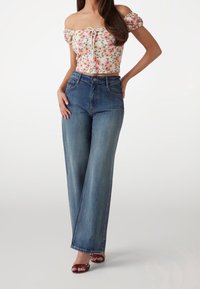 Blå högmidjade vida jeans med medel tvätt, med framfickor och knappstängning, tillsammans med en blommig off-shoulder topp.