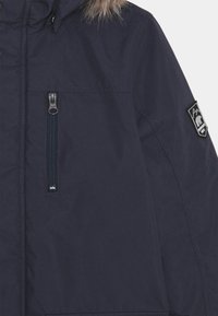 Parka bleu marine avec une capuche bordée de fourrure, dotée d'une poche zippée à l'avant, d'un patch logo et d'un tissu lisse et résistant à l'eau.