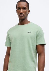 Κοντομάνικη μπλούζα σε μέντα πράσινο με υφή, με στρογγυλή λαιμόκοψη, που φέρει μικρό μαύρο λογότυπο "BOSS" στο στήθος.