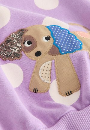 Lilla sweatshirt med prikker, der har et hundedesign. Hunden er applikéet med forskellige teksturer: blomstret, prikket og ensfarvede stoffer.
