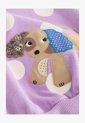 Liliowa bluza z kropkami, z motywem psa. Pies jest aplikowany w różnych fakturach: kwiatowych, w kropki i gładkich tkaninach.