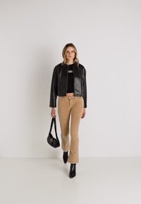Zwarte leren cropped jack over een zwart top, gecombineerd met lichtbruine flared corduroy broek. Model draagt een kleine zwarte handtas.