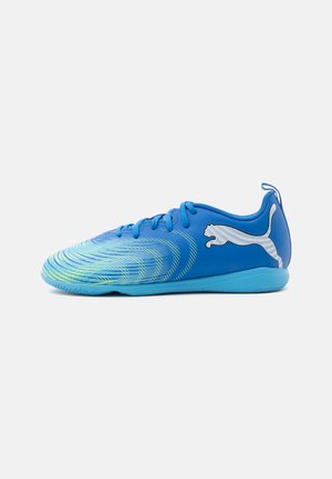 Chaussure de football en salle bleue avec des accents vert clair, des lacets bleus et un logo Puma blanc sur le côté sur fond blanc.