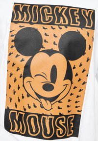Hvid t-shirt med et stort grafik af Mickey Mouse i orange og sort, der blinker og er omgivet af mindre muse-silhuetter.