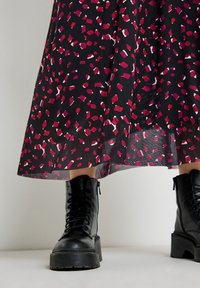 Jupe noire avec un motif abstrait rose et blanc, associée à des bottes noires en cuir à lacets avec des semelles épaisses et une finition texturée.