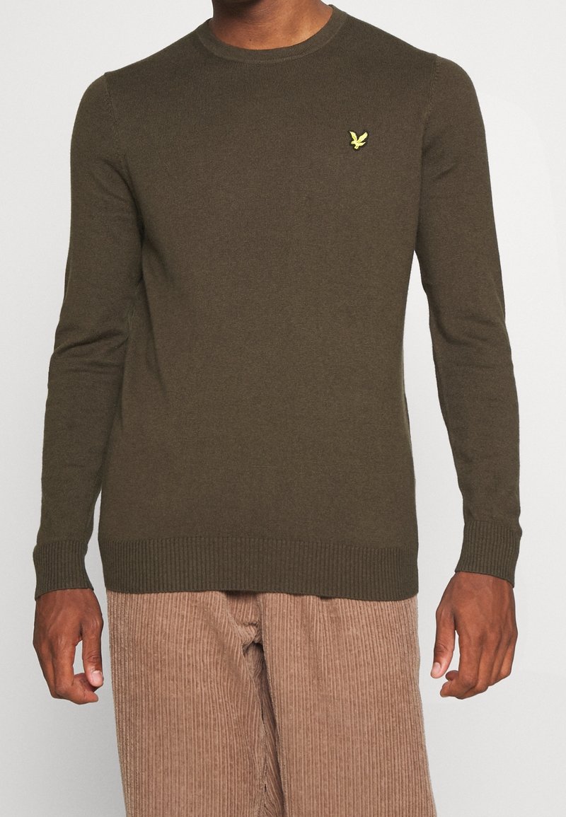 Maglione lavorato a maglia verde oliva con collo rotondo, polsini e orlo a coste, caratterizzato da un piccolo logo giallo sul lato sinistro del petto.