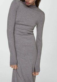 Robe grise à manches longues et ajustée, fabriquée en tissu tricot doux, avec un col haut et des manches longues. Design minimaliste sans motifs visibles.