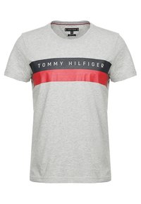 Harmaa lyhythihainen t-paita pyöreällä kaula-aukolla. Siinä on vaakasuoria laivaston sinisiä ja punaisia raitoja, ja edessä on valkoisella "TOMMY HILFIGER" -teksti.