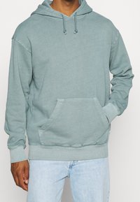 Ljusblågrön hoodie i mjukt tyg med en känguruficka, dragsko i huvan samt ribbade muddar och fåll.