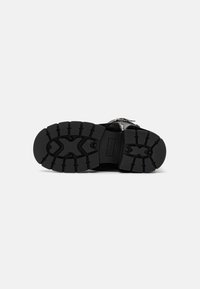 Suela de sandalia negra con una superficie texturizada y patrones de huellas profundos para un mejor agarre, fabricada con un material de goma duradero, diseñada para ofrecer tracción.