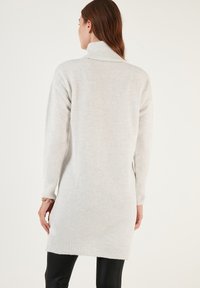 Lys grå strikket tunika sweater med høj krave, lange ærmer, ribbede manchetter og kant. Blød tekstur, slutter ved midten af låret.