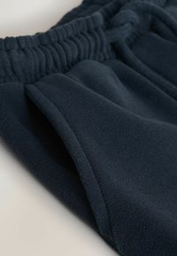 Temno modre fleecej hlače z elastičnim pasom, stranskim žepom in mehko teksturo. Ponašajo se z gladkim zaključkom in detajlom zloženega robu.