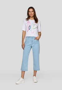 White t-shirt with colorful "Dole" text, light blue cropped pants, and white sneakers. Casual fit with short sleeves and a relaxed design.