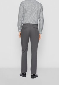 Šedé kalhoty slim fit, vyrobené z bavlněné směsi, s zadními kapsami a hladkým povrchem. Nosí se s vzorovanou košilí.